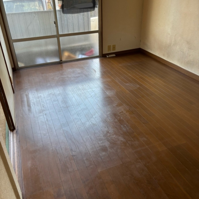 室内のゴミや不用品をすべて撤去し、木目調のフローリングが露わになった片付け後の部屋。消臭・除菌作業により臭気もほぼ感じられない衛生的な状態に改善。
